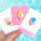 Person holding popsicle needle minders for embroidery in various colors by the pool
