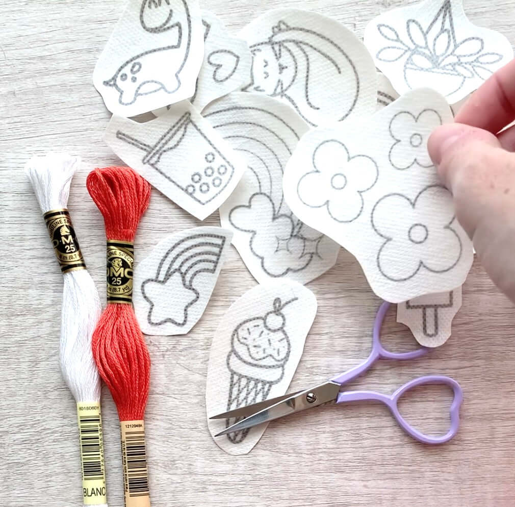 Hand choosing an embroidery pattern from a pile of Stick and stitch embroidery designs