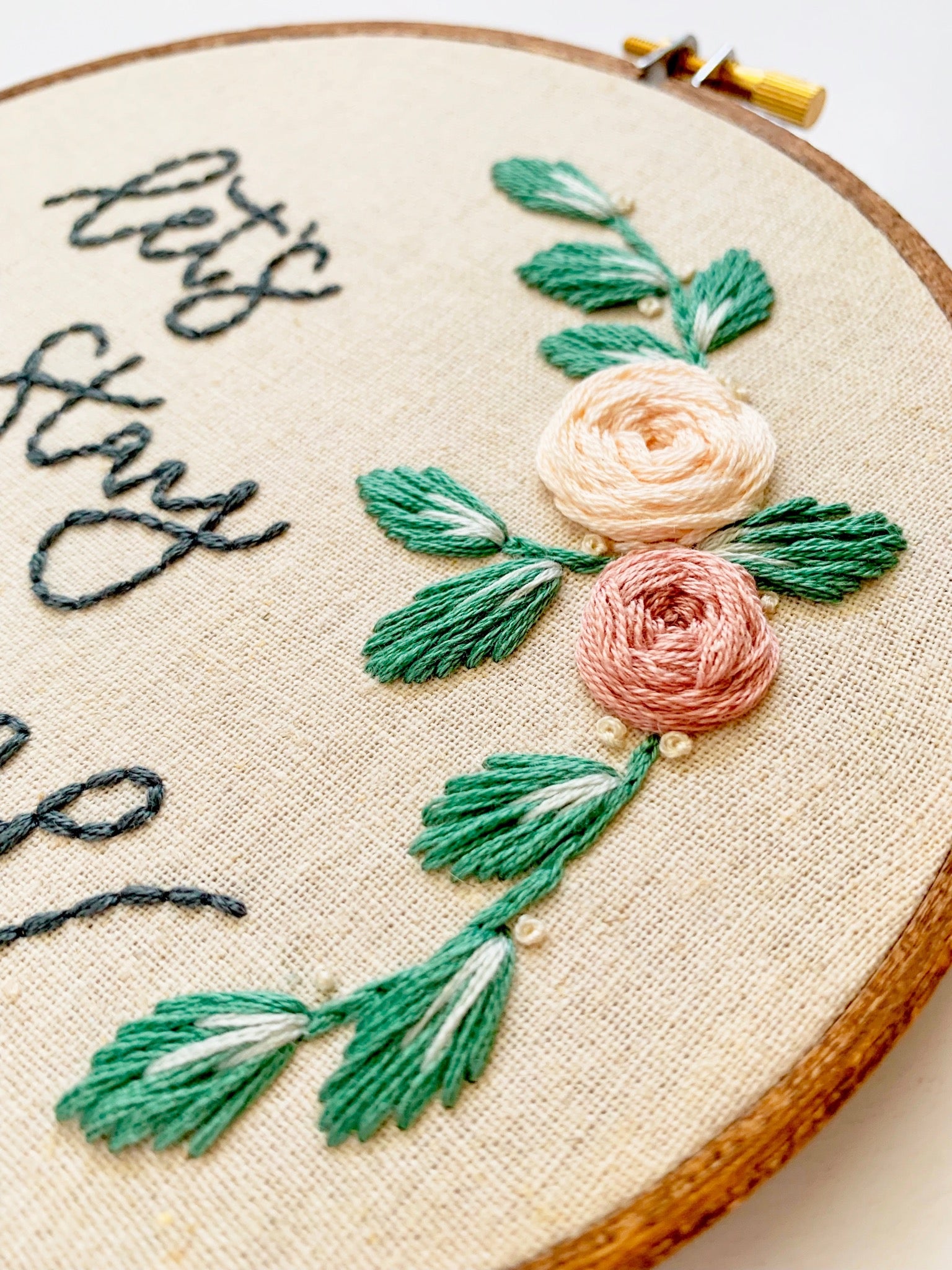 Let's stay home embroidery hoop art with embroidered pink roses and green leaves.