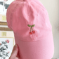 Hand holding up a pink embroidered hat with cherries