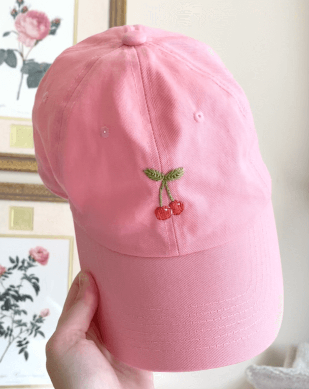 Hand holding up a pink embroidered hat with cherries