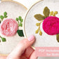 Hand holding two pink rose embroidery hoops