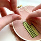 Person sewing a cactus design on pink fabric