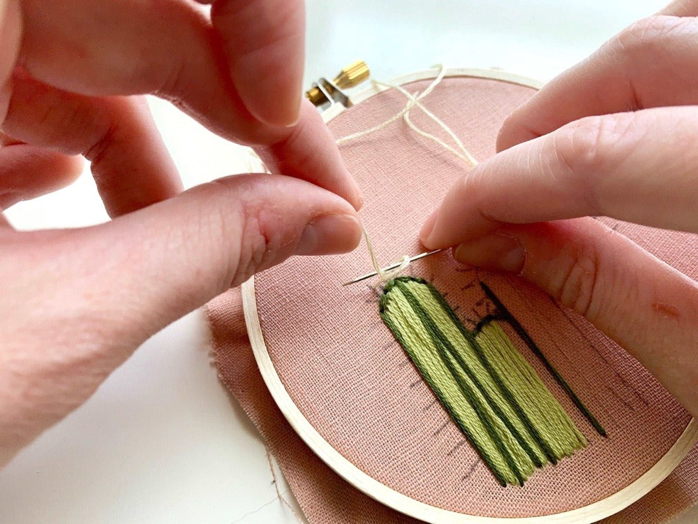 Person sewing a cactus design on pink fabric