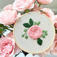 Rose embroidery hoop displayed next to pink roses