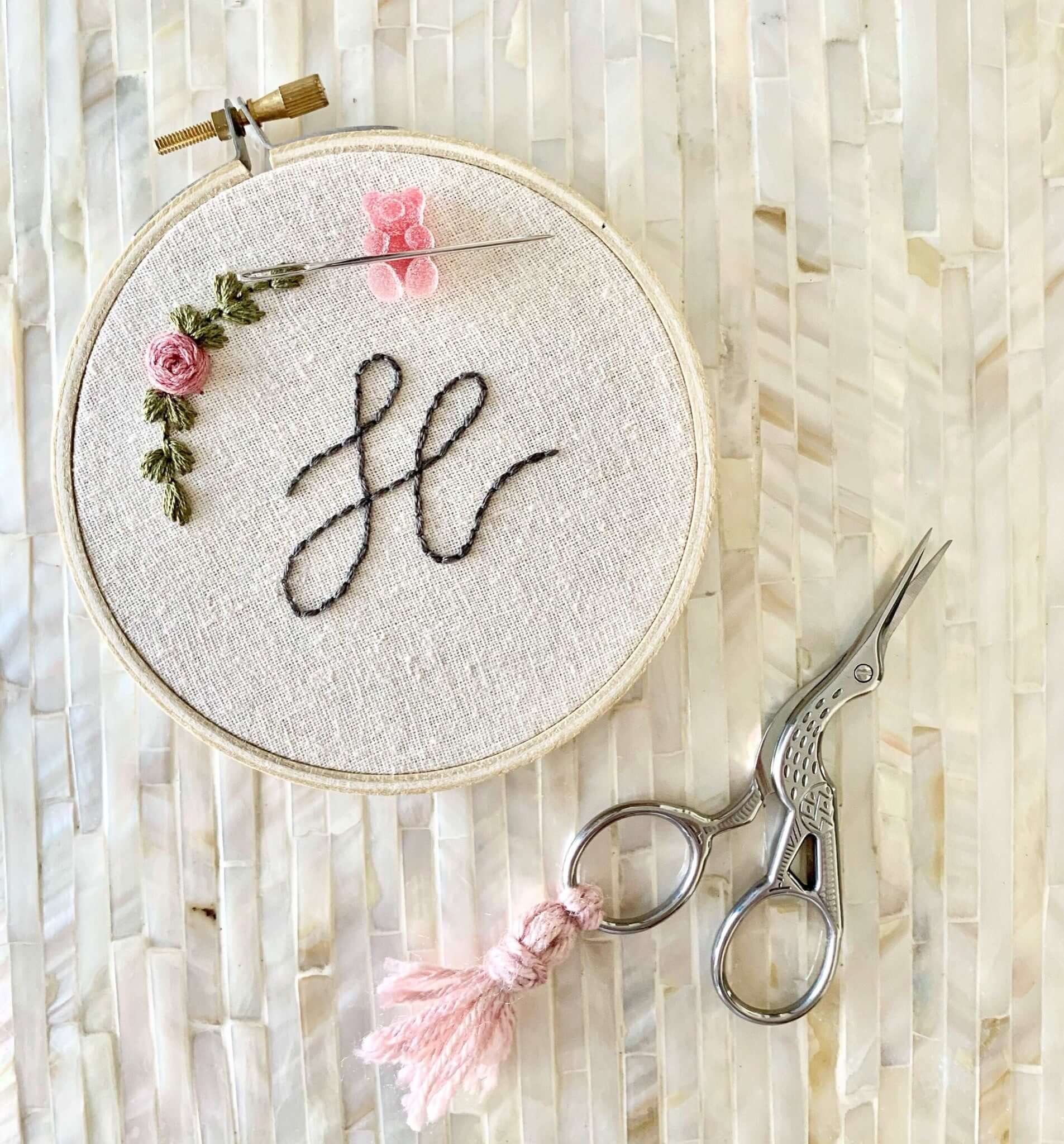 Silver bird sewing scissors with a pink tassel next to an embroidery hoop
