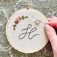 A heart needle minder holding an embroidery needle on an embroidery hoop