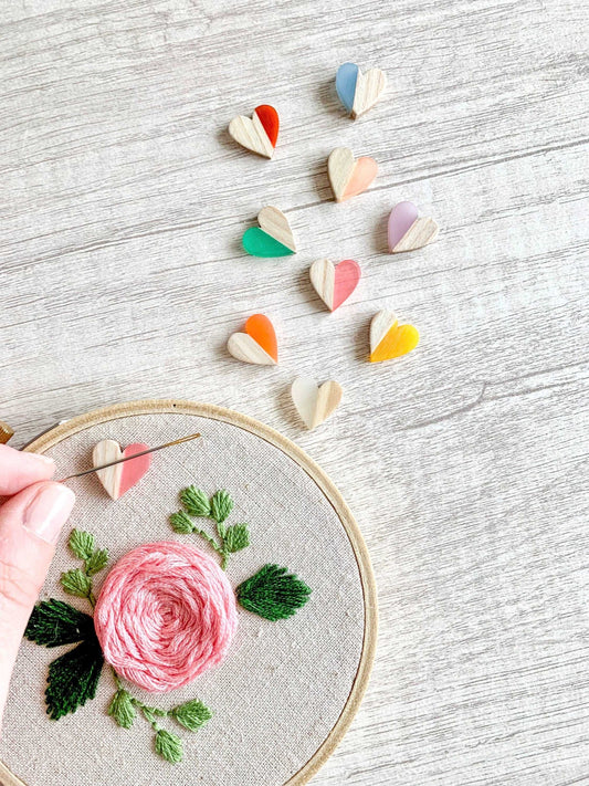 Heart needle minders in various colors next to an embroidered rose hoop