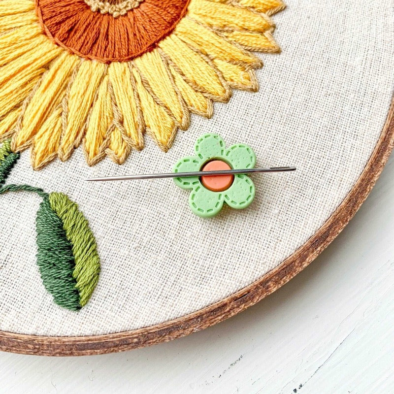 Green flower needle minder holding a needle on a sunflower embroidery design